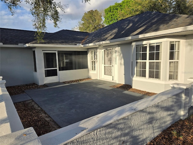 rear view of property with stucco siding and roof with shingles