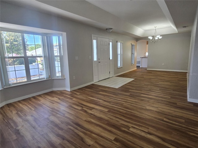 entrance foyer featuring baseboards, a raised ceiling, dark wood-style floors, and a chandelier