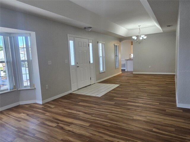 entryway featuring arched walkways, a raised ceiling, baseboards, and dark wood-style flooring