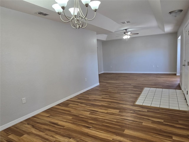 unfurnished room with a tray ceiling, visible vents, baseboards, and wood finished floors