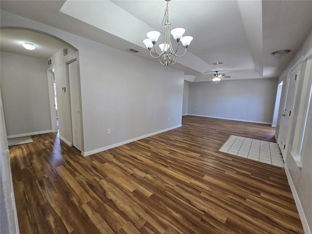 unfurnished room featuring visible vents, dark wood-type flooring, baseboards, a tray ceiling, and arched walkways