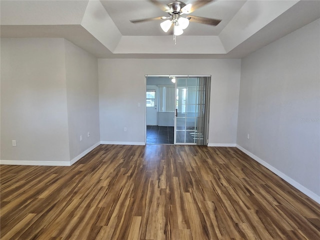 empty room featuring dark wood-style floors, baseboards, and a tray ceiling