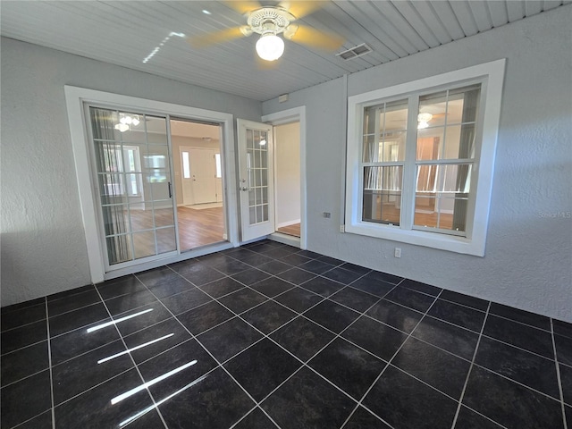 spare room with dark tile patterned flooring, a textured wall, visible vents, and ceiling fan