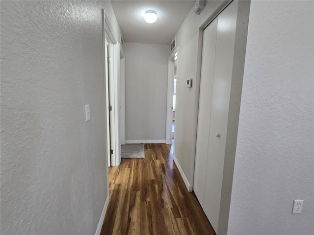 corridor with visible vents, baseboards, a textured wall, and wood finished floors