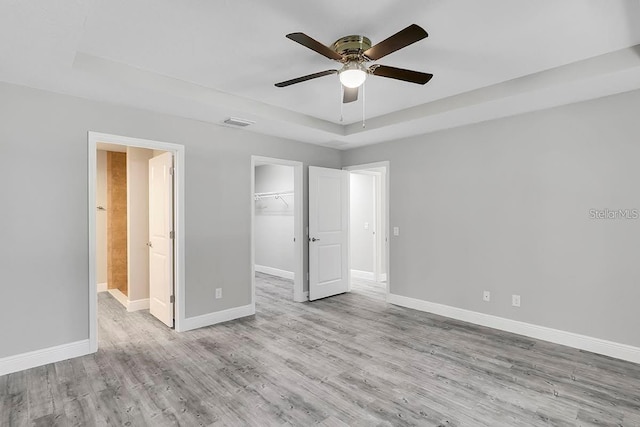 unfurnished bedroom featuring a spacious closet, a tray ceiling, baseboards, and wood finished floors