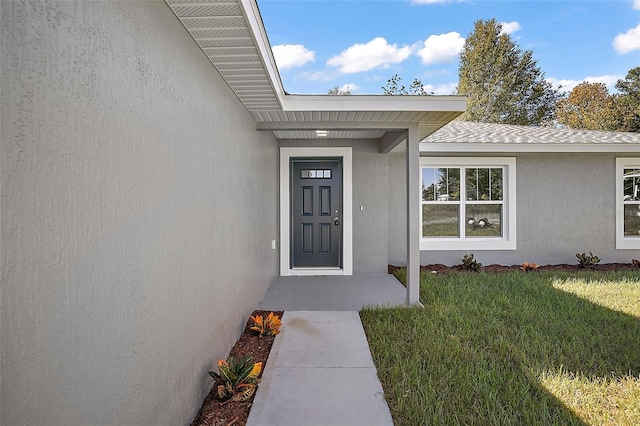 doorway to property featuring a lawn and stucco siding