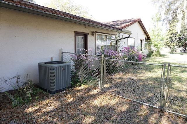 view of home's exterior with fence, a tile roof, central AC unit, stucco siding, and a gate