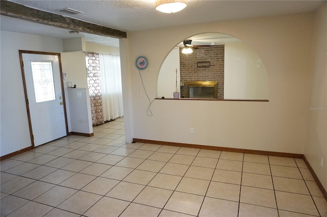 interior space with baseboards, light tile patterned floors, a fireplace, a textured ceiling, and a ceiling fan