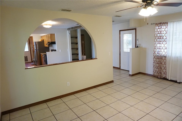 interior space with visible vents, a ceiling fan, a textured ceiling, freestanding refrigerator, and arched walkways