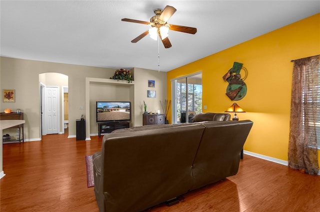 living room featuring arched walkways, baseboards, ceiling fan, and wood finished floors