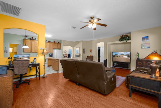 living area with arched walkways, visible vents, light wood-type flooring, and a ceiling fan