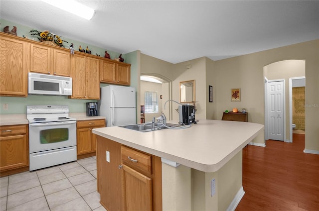 kitchen featuring a kitchen island with sink, white appliances, arched walkways, light countertops, and light tile patterned floors