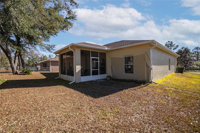 rear view of property with stucco siding, fence, a yard, and a sunroom