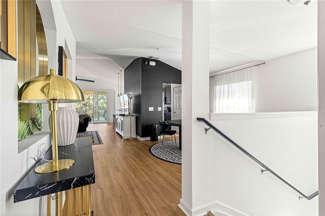 hallway featuring baseboards, vaulted ceiling, an upstairs landing, wood finished floors, and a textured ceiling