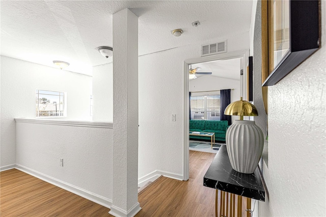 hall with visible vents, a textured ceiling, a textured wall, and wood finished floors