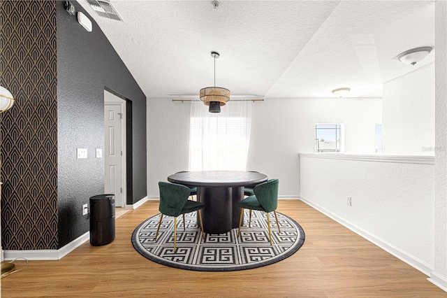 dining space featuring visible vents, a textured ceiling, wood finished floors, baseboards, and vaulted ceiling