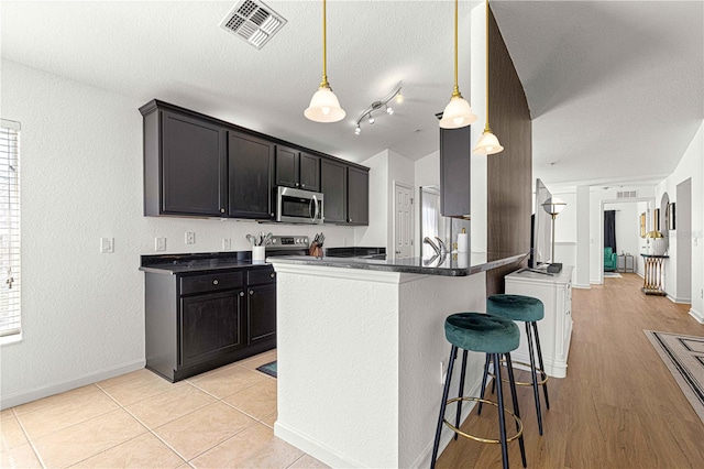 kitchen with dark countertops, visible vents, appliances with stainless steel finishes, and a breakfast bar area