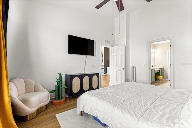 bedroom featuring visible vents, ensuite bathroom, wood finished floors, a towering ceiling, and ceiling fan