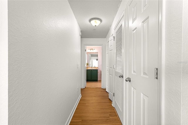 corridor with a textured ceiling, wood finished floors, baseboards, and a textured wall