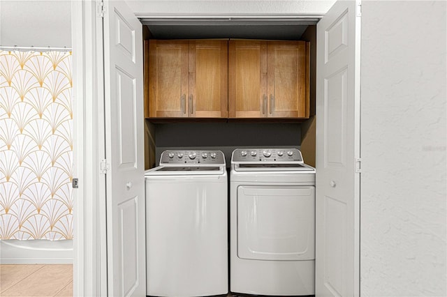 clothes washing area featuring tile patterned floors, cabinet space, and washing machine and dryer