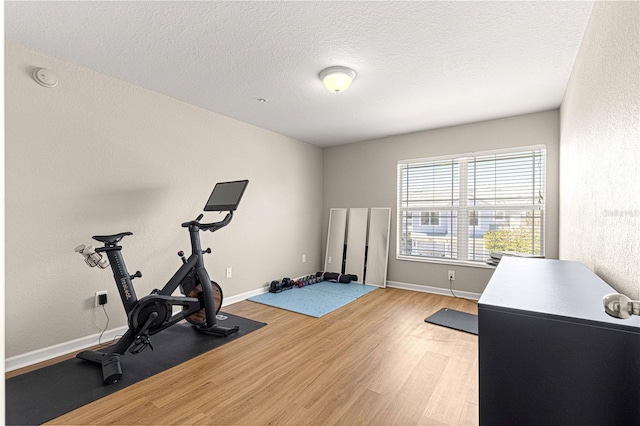 exercise area featuring light wood-style flooring, a textured ceiling, baseboards, and a textured wall