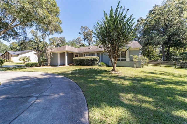 ranch-style home featuring a front lawn, concrete driveway, fence, and stucco siding