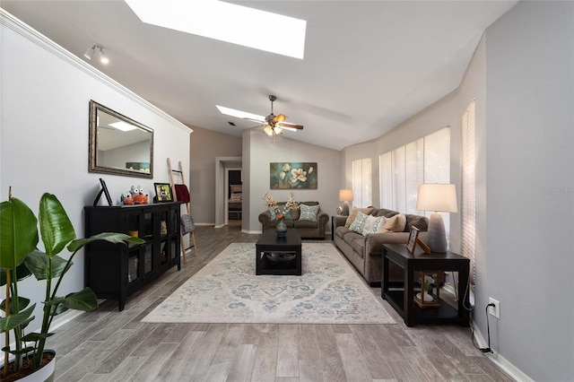 living area with a ceiling fan, lofted ceiling with skylight, wood finished floors, and baseboards