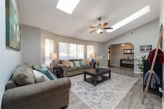 living room featuring visible vents, a ceiling fan, arched walkways, light wood-style floors, and a skylight