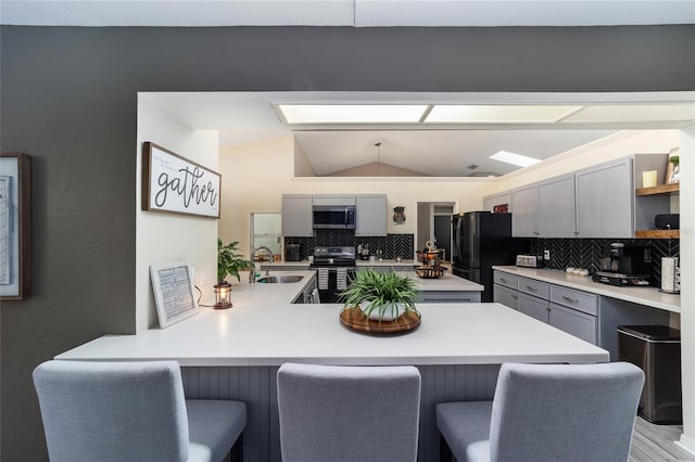 kitchen featuring a sink, a peninsula, appliances with stainless steel finishes, a breakfast bar area, and lofted ceiling