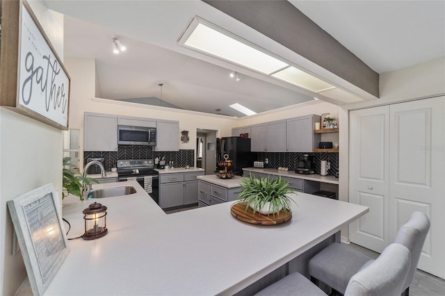 kitchen with a breakfast bar area, open shelves, gray cabinets, a sink, and stainless steel appliances