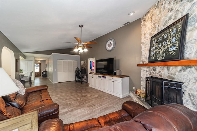 living room featuring visible vents, lofted ceiling, a fireplace, wood finished floors, and arched walkways