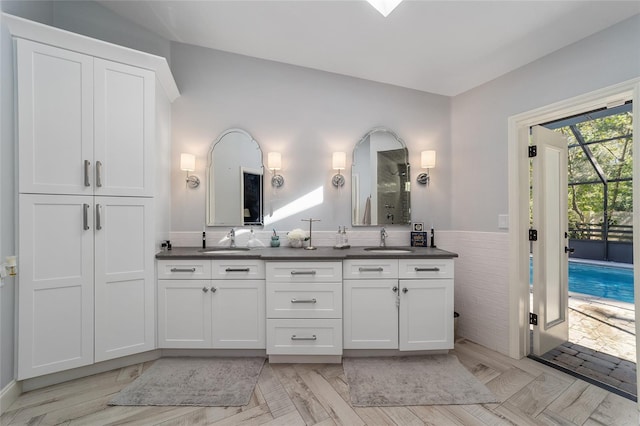 full bathroom with double vanity, walk in shower, a wainscoted wall, and a sink