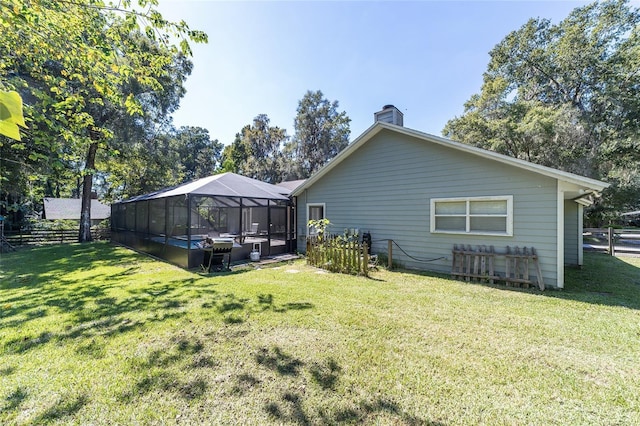 back of property featuring glass enclosure, a lawn, fence, and a chimney