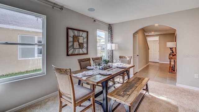 dining room with baseboards, arched walkways, and light carpet