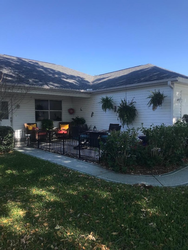 view of side of home with a yard, fence, and roof with shingles