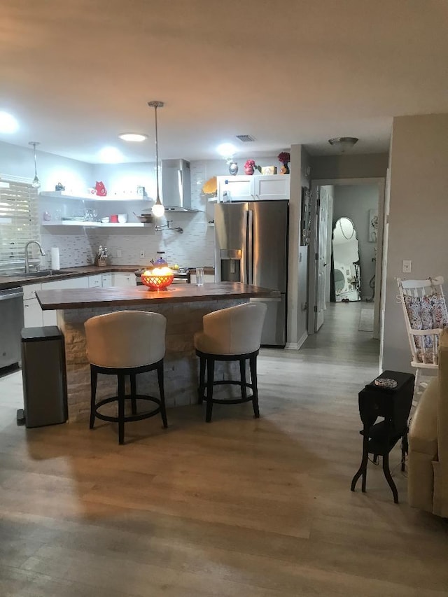 kitchen with a sink, appliances with stainless steel finishes, wall chimney exhaust hood, and white cabinets