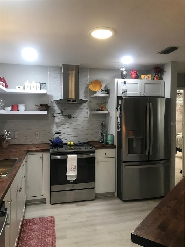 kitchen with open shelves, butcher block countertops, stainless steel appliances, visible vents, and wall chimney range hood