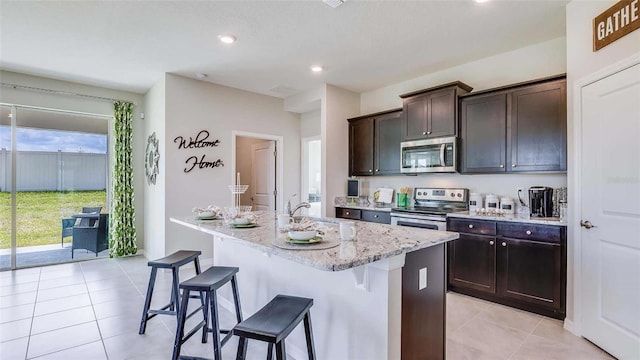 kitchen with a kitchen island with sink, a sink, a kitchen breakfast bar, stainless steel appliances, and light stone countertops