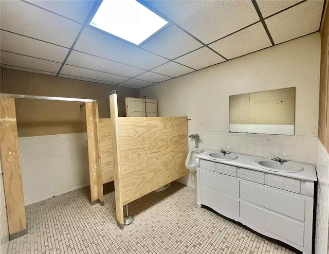 unfurnished bedroom featuring a drop ceiling, wainscoting, tile walls, and a sink