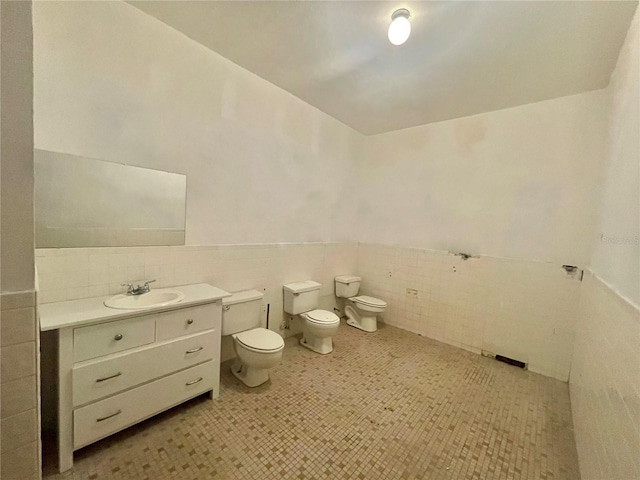 bathroom with vanity, a bidet, a wainscoted wall, tile walls, and toilet