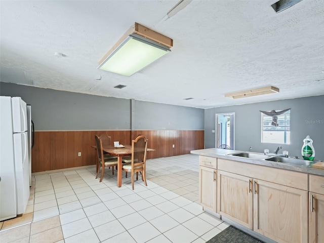 kitchen featuring light brown cabinets, wainscoting, freestanding refrigerator, and a sink