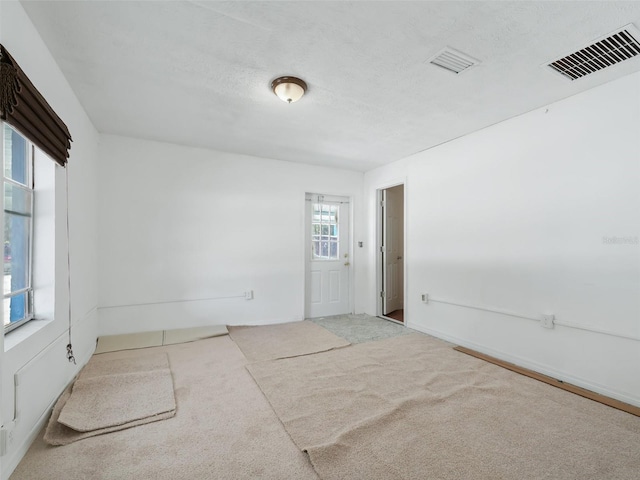 carpeted spare room with visible vents and a textured ceiling