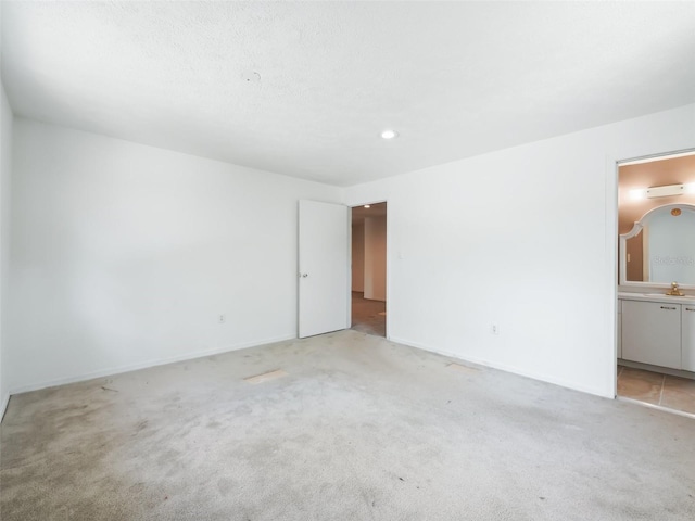 unfurnished bedroom featuring a sink, light carpet, and ensuite bath