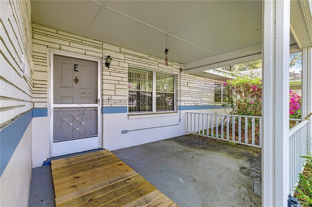 view of exterior entry with a porch and brick siding