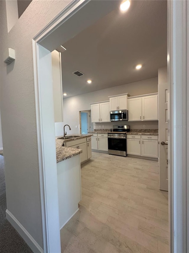 kitchen with a sink, stainless steel appliances, light wood-style floors, white cabinets, and light stone countertops