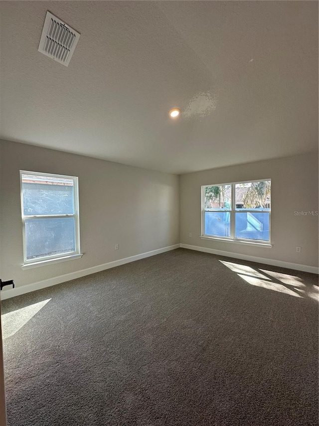 empty room featuring baseboards, visible vents, dark colored carpet, and a healthy amount of sunlight