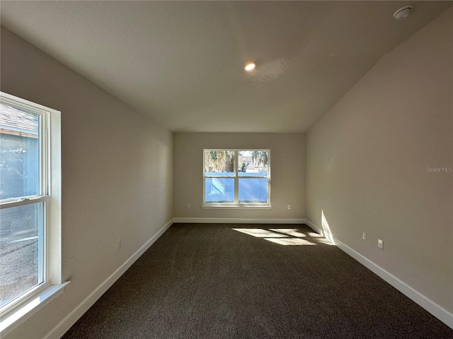 unfurnished room with dark carpet, lofted ceiling, and baseboards