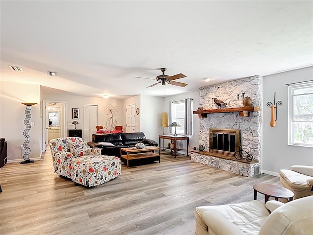 living room with a fireplace, a ceiling fan, visible vents, and light wood finished floors