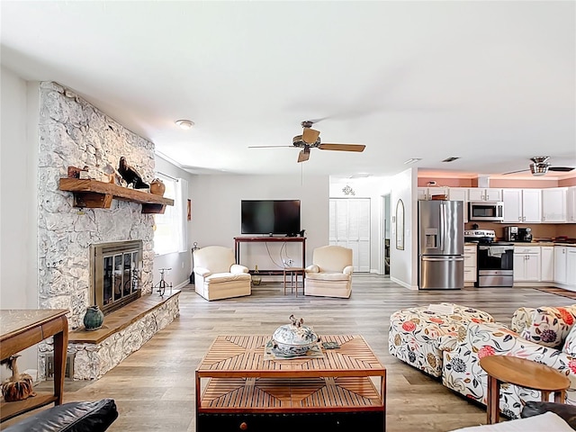 living room featuring light wood-style flooring, baseboards, a stone fireplace, and ceiling fan