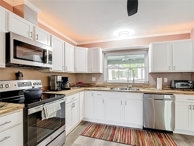 kitchen with a sink, crown molding, light wood finished floors, and stainless steel appliances